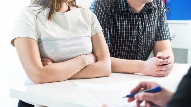 Two people seated beside each other while a third person takes notes.