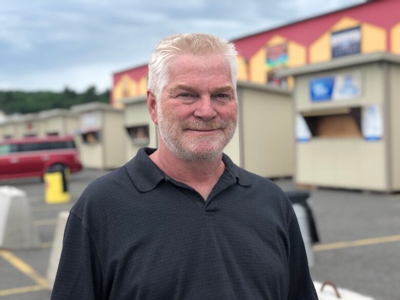 A man stands outside in a parking lot wearing a black polo shirt.