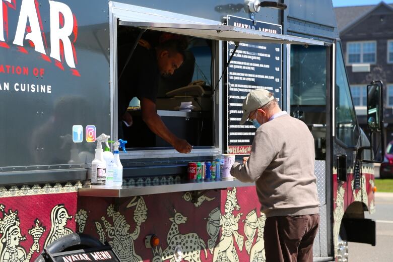 A black food truck with red and yellow art on it. We see a man inside the truck window and a man outside.