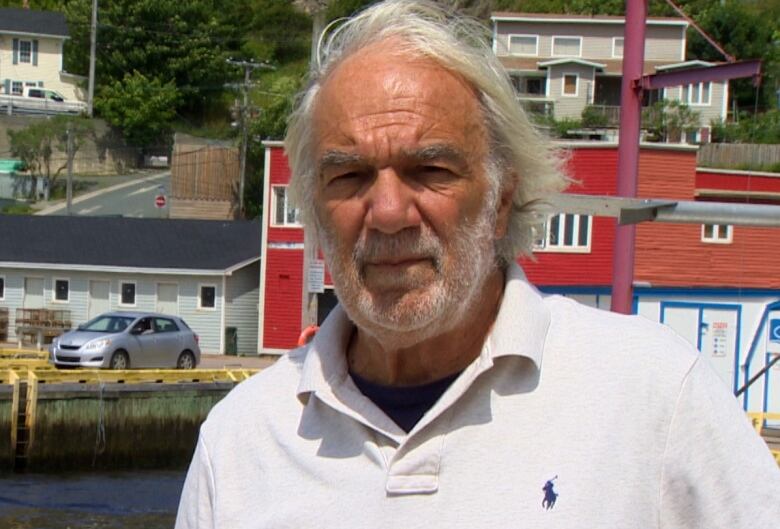 Bill Montevecchi stands on a wharf with boats and houses behind him