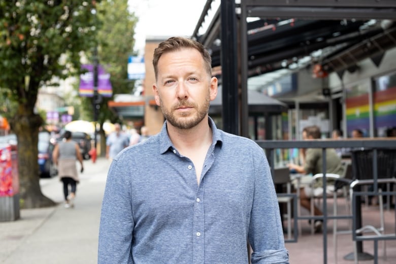 A white man wearing a blue shirt poses on a busy street.