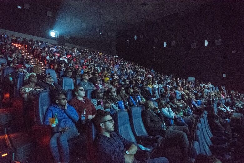 An audience watches a movie in a darkened theatre.