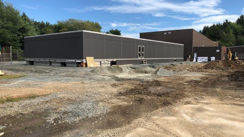 A long grey building sits on gravel.