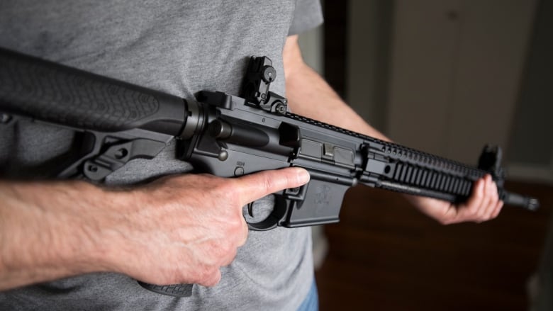 A man holds an AR-15 rifle.