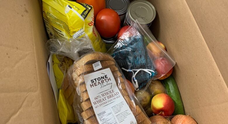 Cardboard box holding a loaf of bread, fruit, vegetables, canned goods and pasta.