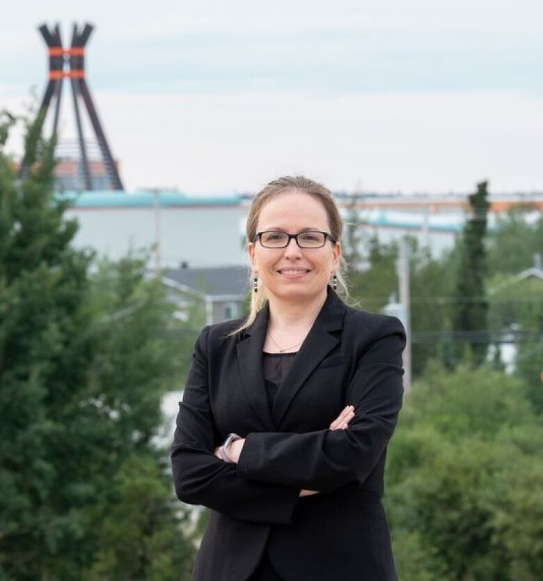 A Cree woman stands on a hill with downtown Chisasibi in the background.