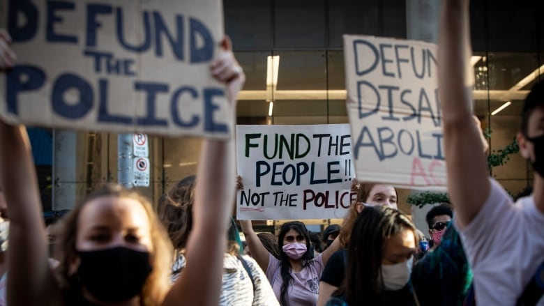 A group of protesters holding up  signs. One sign reads 