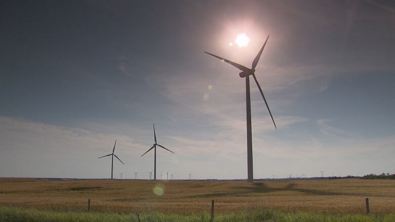 Three windmills in a row on the flat horizon of a field in Alberta.