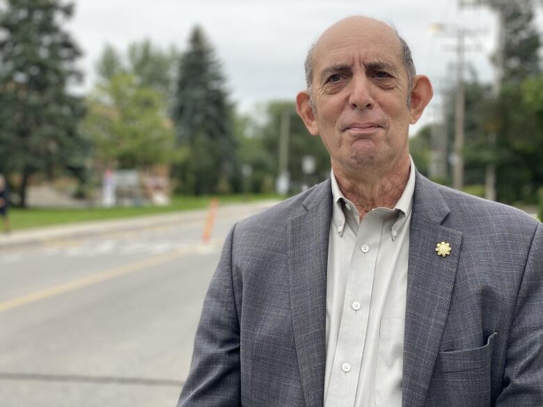 Marvin Rotrand stands on the street wearing a grey suit with a white shirt.