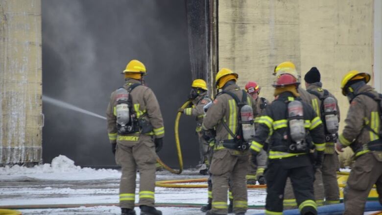 Seven firefighters putting out a fire with a firehose.