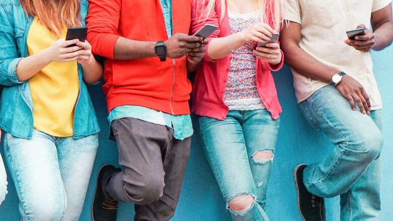 A row of four people, each using smartphones, lean against a bright blue wall.