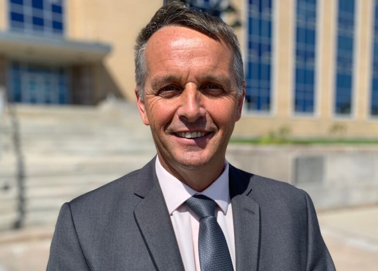 A smiling man wearing a suit stands in front of Confederation Building.