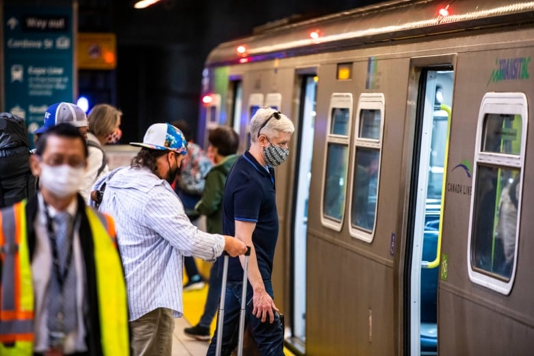 A group of people wearing masks enter a SkyTrain.