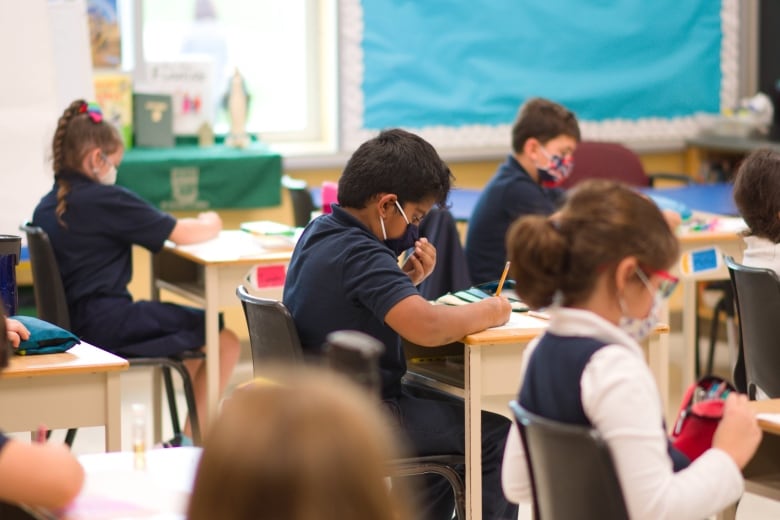 Children sit at classroom desks wearing masks.