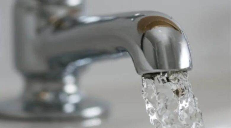 A closeup of a silver faucet spewing water into a sink