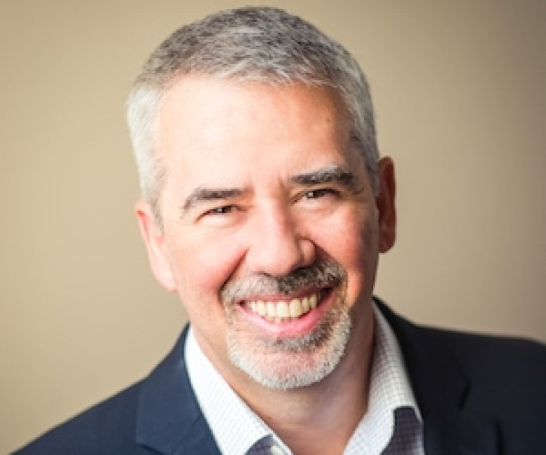 A smiling man in front of a beige background