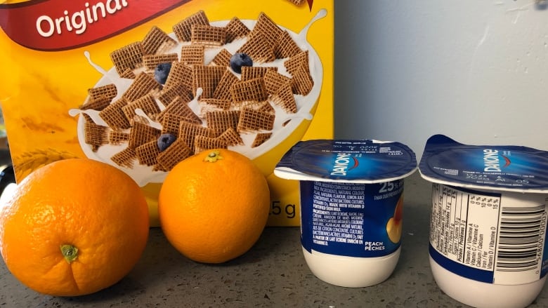 Yellow cereal box, two oranges and two small tubs of yogurt shown.