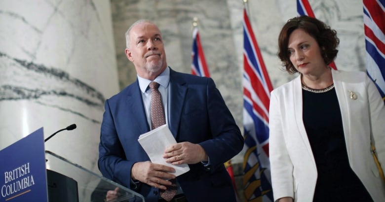 A man in a blue suit and a young woman in a white jacket stand near a podium