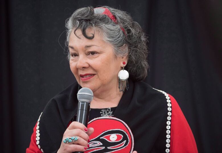 A woman in red and black speaks into a microphone.