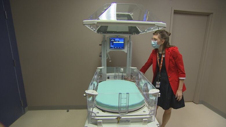 Woman at side of baby-sized hospital bed. 