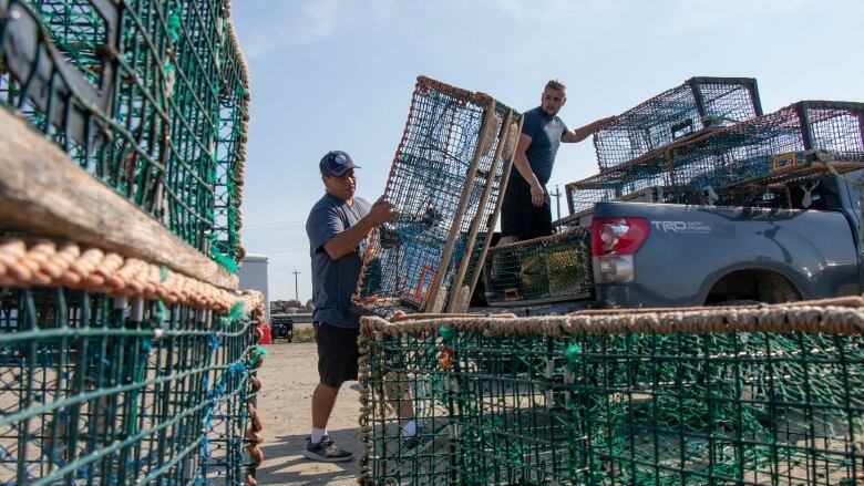 A man holds an empty lobster trap near a pickup truck.