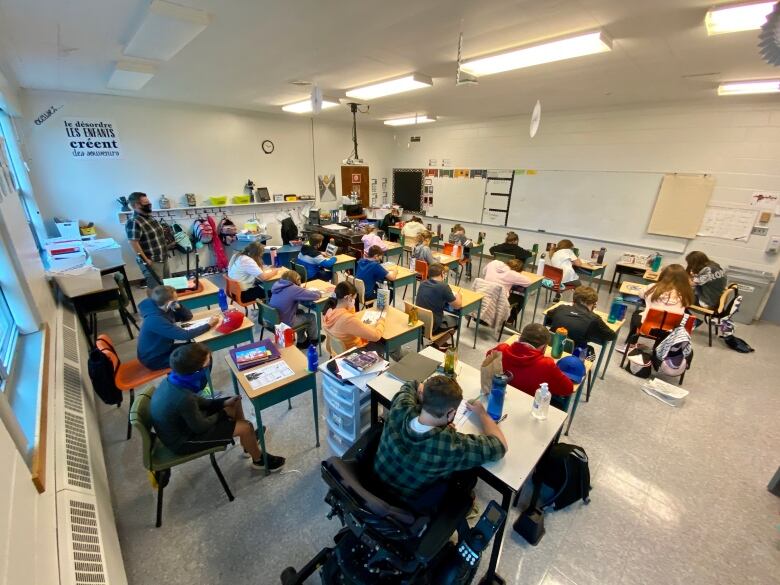 Students and a teacher, all wearing masks, sit in a classroom.