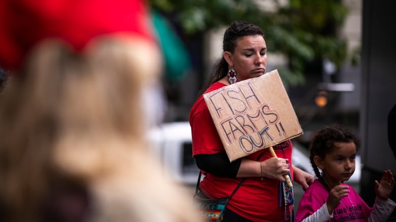 Woman holds hand made sign on card board that reads 