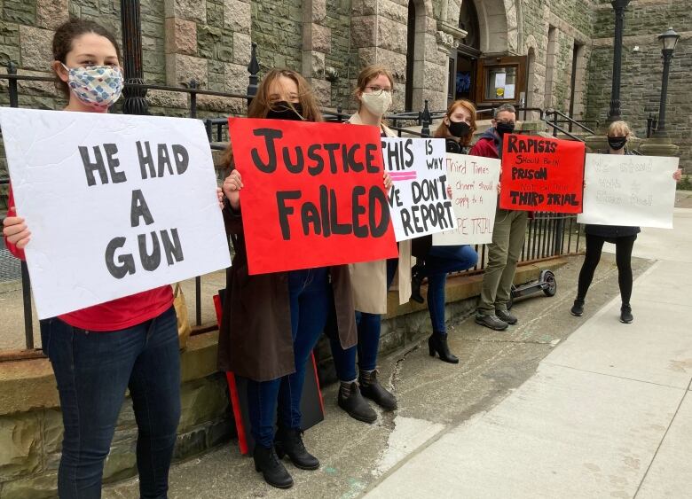 Women wearing masks hold signs outside a brick building. 