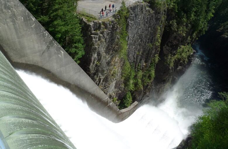 Flowing water off a dam, with spectators visible well in the background.