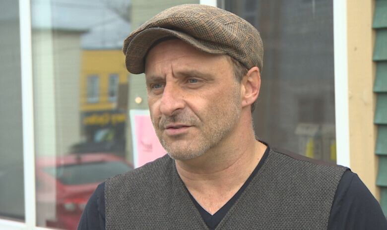 A man wearing a vest and a hat stands outside a St. John's food bank.