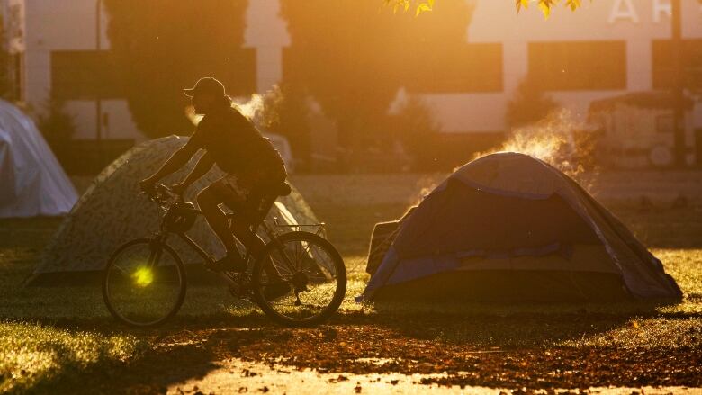 A person bikes past a tent.