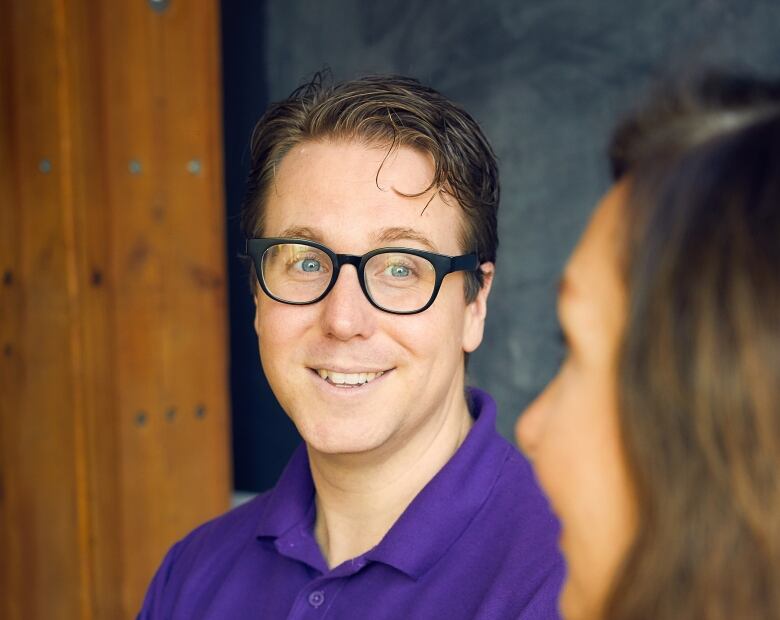 A man in a purple shirt and glasses looks to the side.