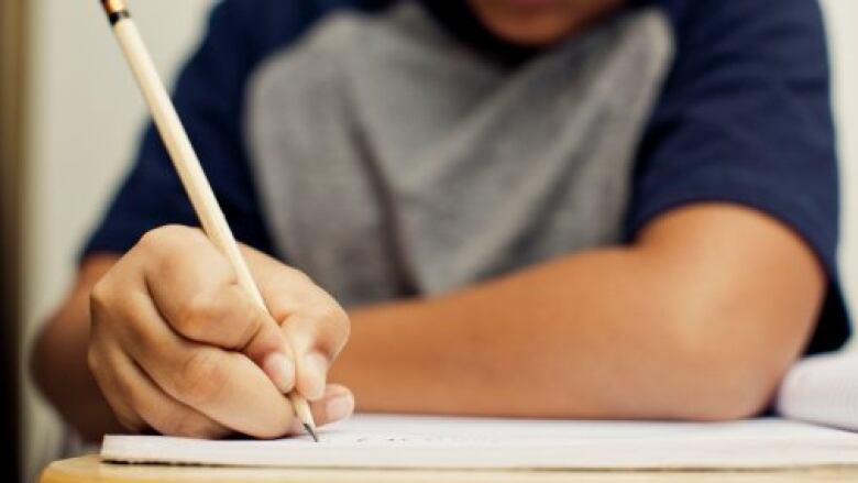 A close-up of a male student sitting at a desk holding a pencil over a piece of paper