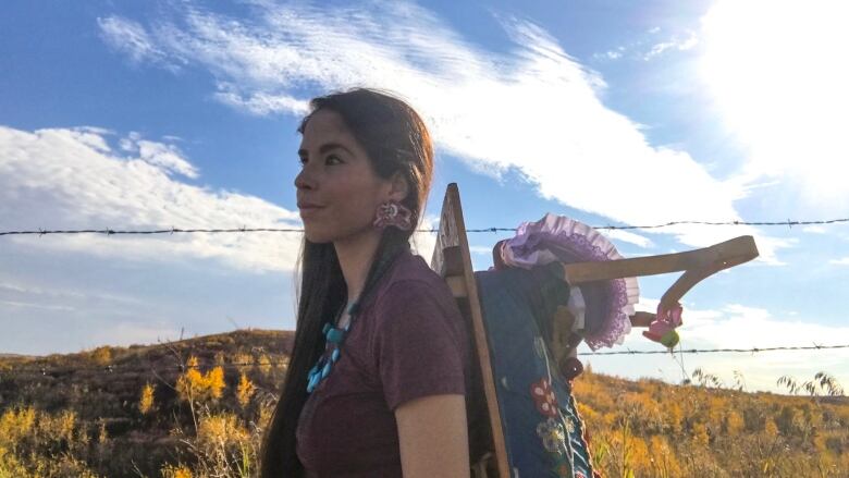 Woman standing in nature with a baby bundle on her back, she has long dark hair