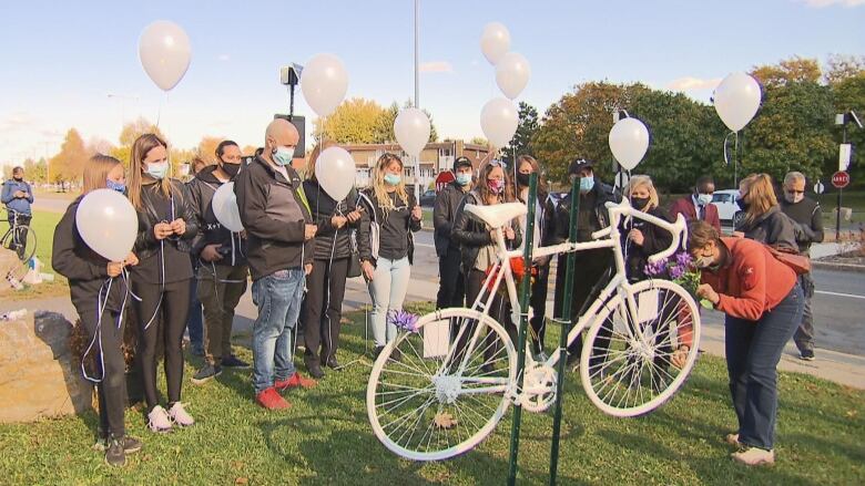 People gathering around a bike painted white and white balloons. 