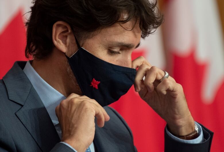 A man in a suit adjusts a medical face mask.