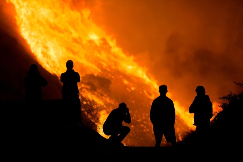 Five people silouetted by a raging wildfire in the background. 