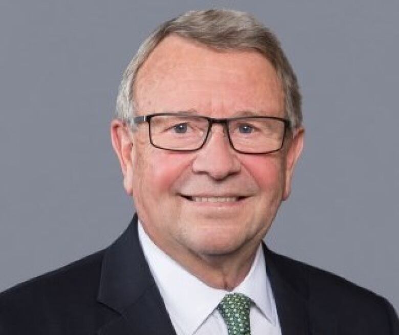 A portrait of a man wearing a black suit and green tie.