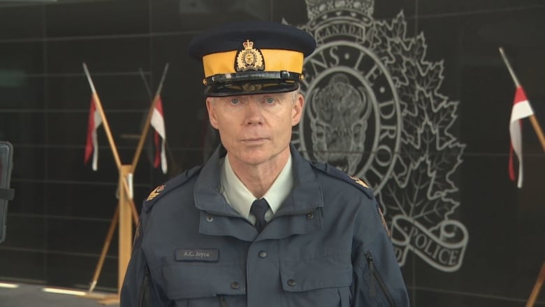 A white man with grey hair and light blue eyes is wearing a dark blue police jacket and cap.