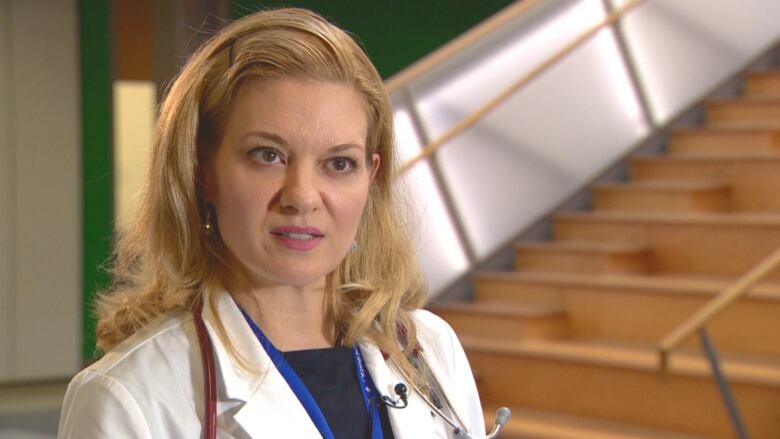 A blonde woman in a white doctor's coat looks at the camera. 