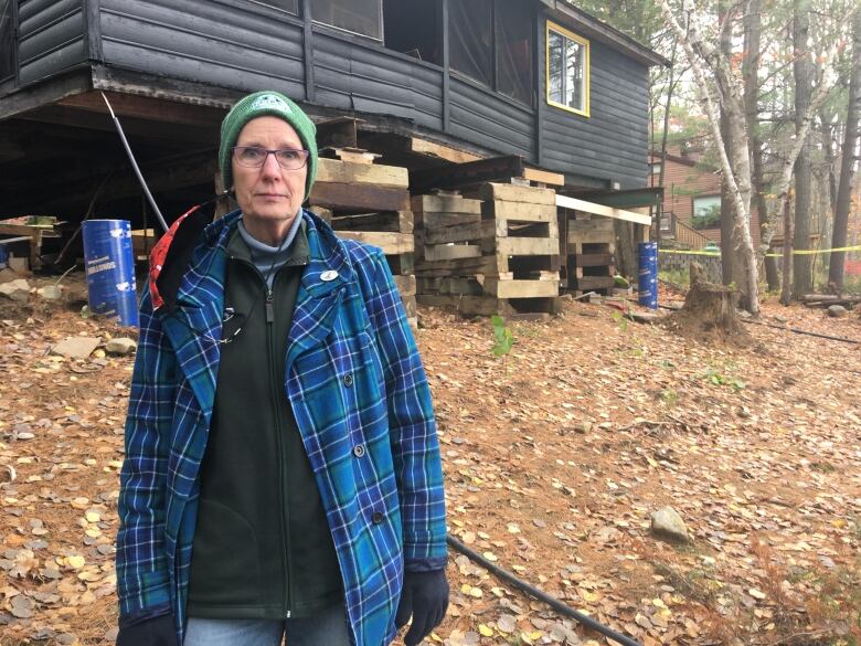 A woman stands in front of a cottage that's raised up precariously on wooden blocks two metres off the ground.