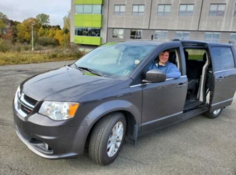 A man sits in the driver's seat of a mini-van.