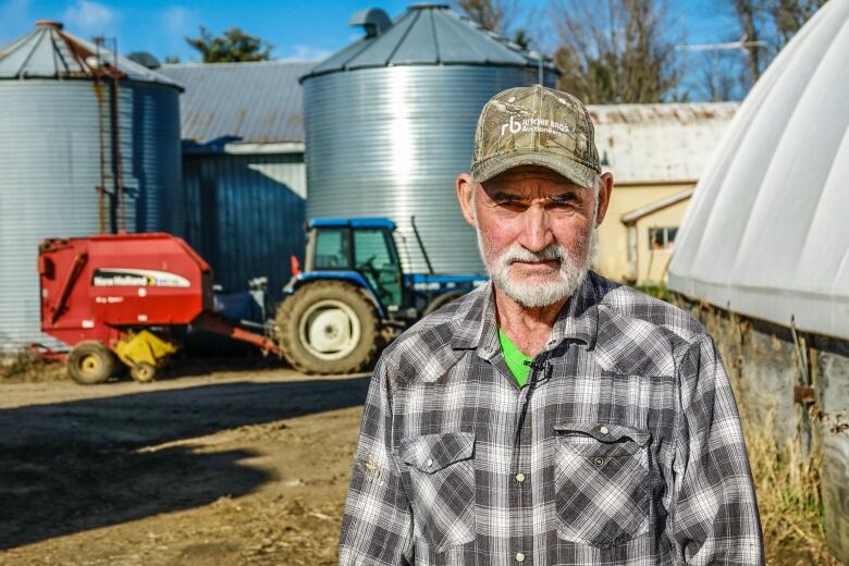 A man in a ball cap and plaid short poses for a photo outside on a farm.