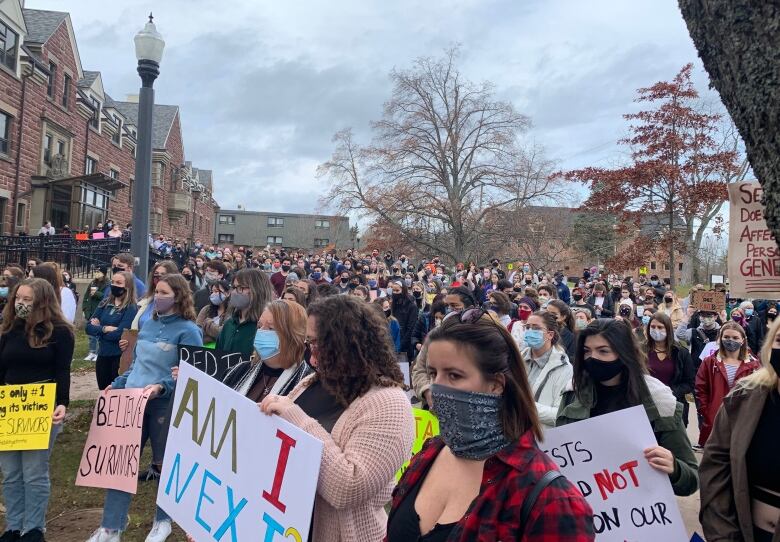 A group of dozens of young people hold handwritten signs. 