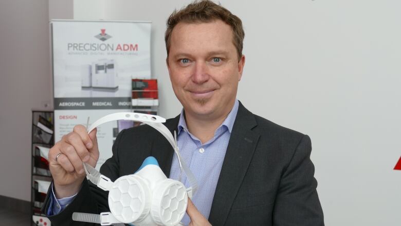 A man wearing a suit holds up a white respirator.