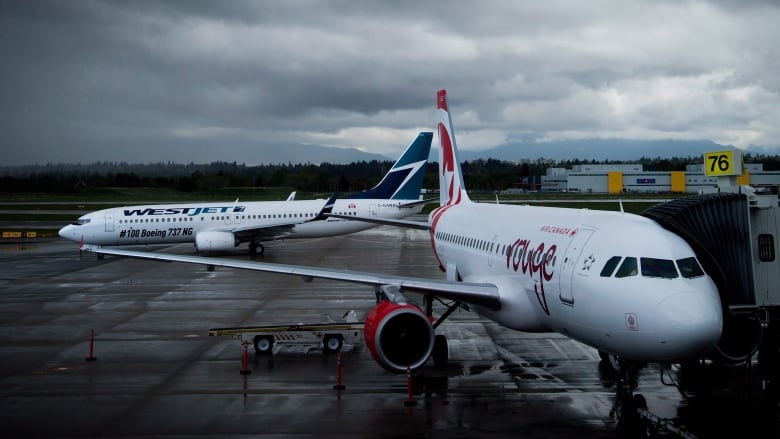 Two airplanes sit on the tarmac at an airport.