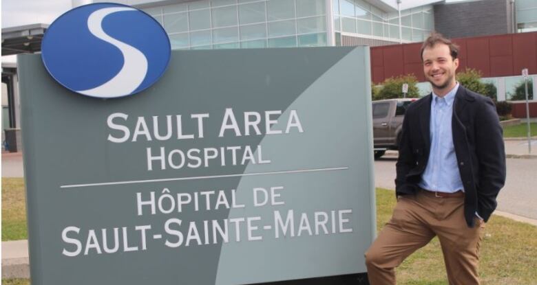 A man standing outside next to a sign that says Sault Area Hospital.