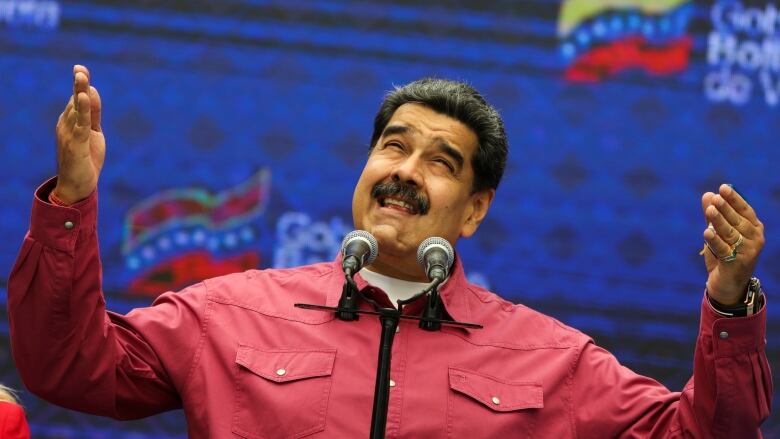 Maduro stands with his hands raised in a red shirt in front of a microphone. 