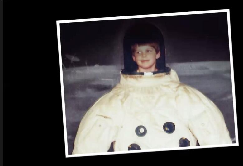 Astronaut Jeremy Hansen, as a kid, poses behind a cut-out of an astronaut suit.