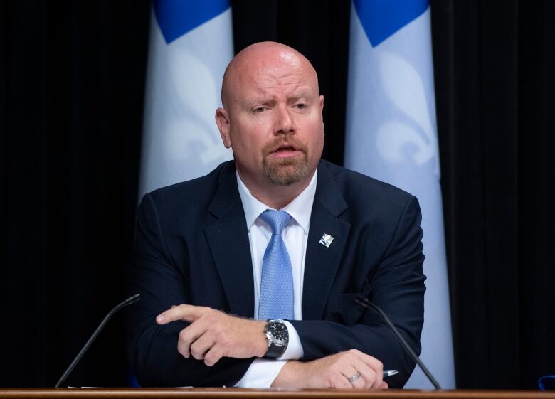 Ian Lafrenire speaking at a conference flanked by Quebec flags. 